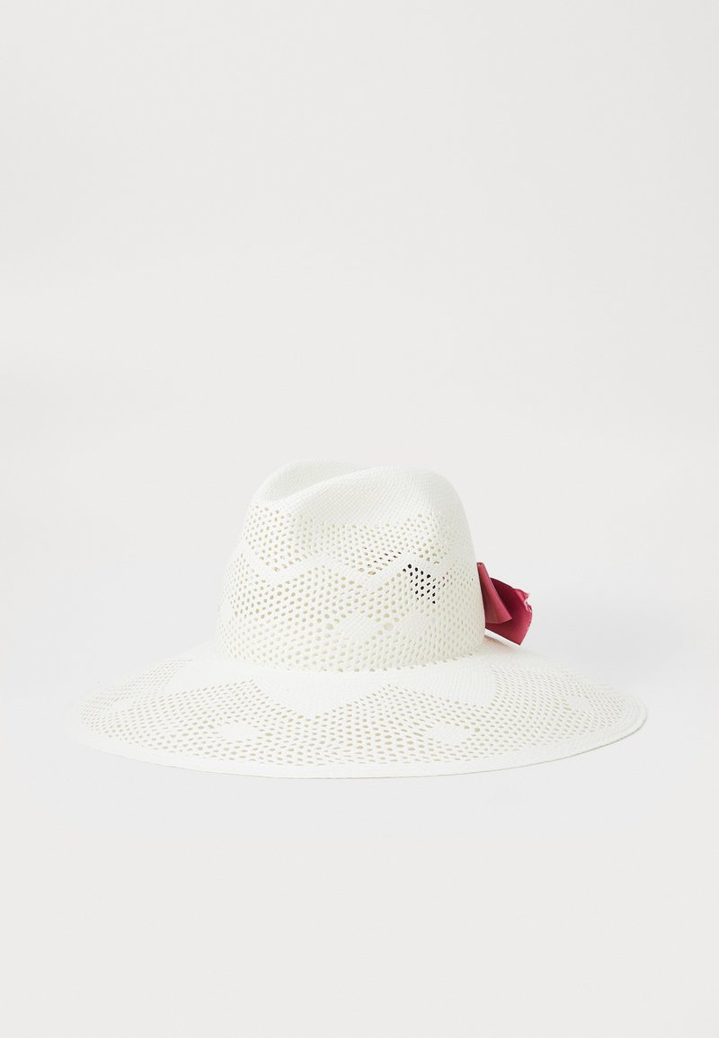 White wide-brimmed hat with a perforated design and a pink ribbon accent on the side. Made from lightweight material, featuring a smooth texture.