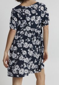 Námořnické šaty s bílým květinovým vzorem, krátkými balónovými rukávy, V-výstřihem a nařaseným pasem, s volnou sukní z texturované látky.