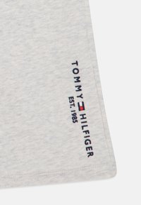 Tessuto di cotone grigio chiaro con una finitura texture. Presenta "TOMMY HILFIGER" e "EST. 1985" ricamati con filo blu navy e rosso.