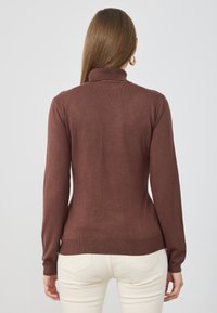 Brūns, ribots turtlenecks džemperis ar garām piedurknēm. Pieguļošs dizains ar gludu tekstūru un maigu apdari. Nav ievērojamu rakstu vai aparatūras.