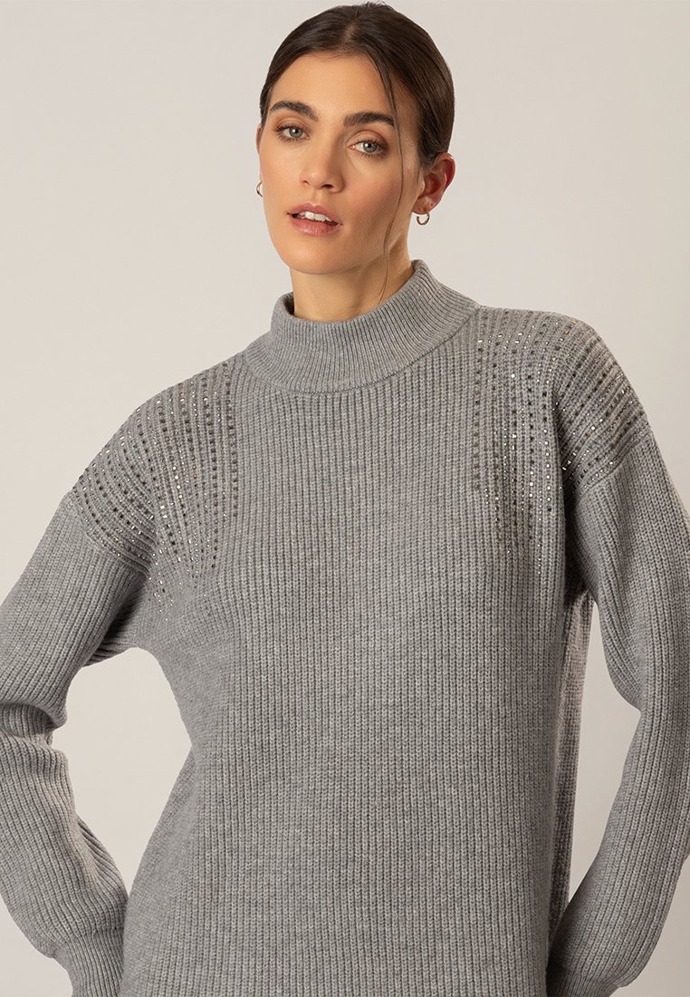 Grauer Strickpullover mit hohem Kragen, gerippter Textur und subtilen Glitzerdetails an den Schultern. Lange Ärmel vervollständigen das Design.