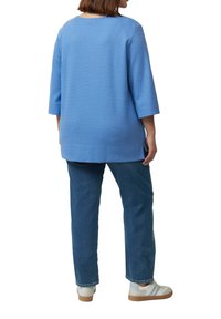 Blauw gestructureerd sweater met driekwart mouwen, gecombineerd met blauwe jeans en witte sneakers; de achteraanzicht toont een relaxte pasvorm en een eenvoudig ontwerp.