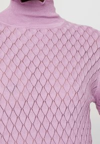 Pull roulé en maille violet clair avec un motif ajouré en forme de losange.