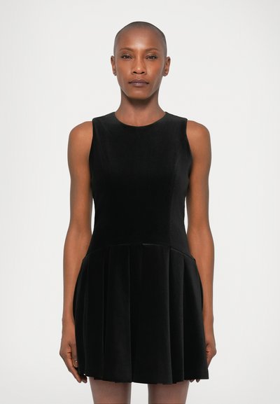 Zwarte mouwloze jurk van fluweelstof, met een aansluitende lijfje en een uitlopende geplooide rok. Glad textuur, minimalistisch ontwerp en lengte boven de knie.