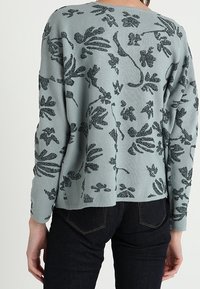 Langarm, strukturiertes, hellblaues Sweatshirt mit einem schwarzen Blumenmuster, das einen entspannten Schnitt und einen abgerundeten Saum aufweist.