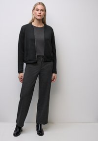 Svart bomberjacka med dragkedja fram, kombinerad med mörkgrå vida byxor. Slät tyg med subtil struktur och fickor. Svarta ankelboots.