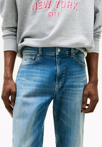 Jeans azzurri in taglio dritto con una finitura sbiadita. Le caratteristiche includono una chiusura con bottone, cinque tasche e un piccolo logo sulla tasca anteriore.