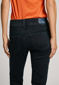 Zwarte denim jeans met een slim fit, voorzien van achterzakken en subtiele stikdetails. Gemanierd met een oranje shirt.