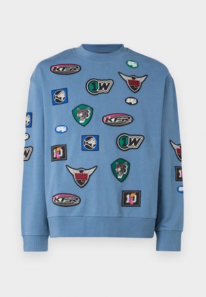 Sweatshirt albastru cu guler rotund, decorat cu diverse petice colorate, inclusiv motive de animale și logo-uri. Mâneci lungi și mansete ribbate.