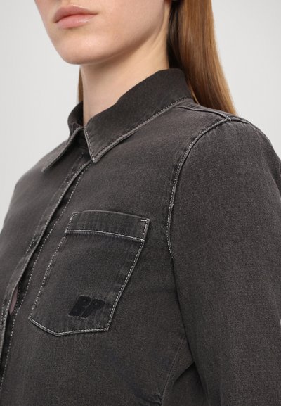 Camisa de ganga preta com colarinho clássico, bolso frontal, costura branca contrastante e detalhe do logótipo da marca no bolso.