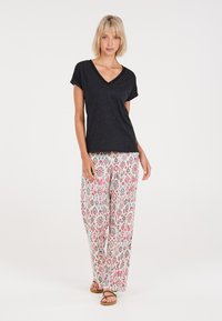 T-shirt nera con scollo a V e maniche corte, abbinata a pantaloni larghi e stampati con disegni floreali rosa e blu su sfondo bianco.