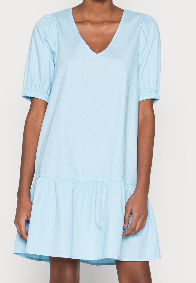 Svetle modré šaty s krátkým rukávem a výstřihem do V, s nařasenými rukávy a rozšířeným, vrstveným lemem. Vyrobeno z lehkého materiálu se hladkým povrchem.