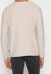 Beiges Langarmshirt mit gerippter Struktur, rundem Ausschnitt und geradem Schnitt. Es verfügt über eine Naht in der Mitte des Rückens und ein seitliches Etikett.