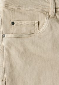 Béžová denimová látka se přední kapsou s kontrastním šitím a klasickým knoflíkovým detailem, která ukazuje texturovaný povrch.