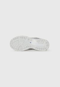 White athletic shoe sole featuring textured rubber with a patterned tread for grip and stability. Smooth accents towards the heel area.