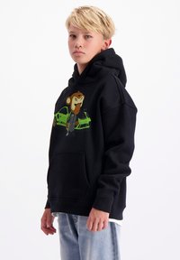 Zwarte hoodie met een cartoon aap grafiek in groen en bruin, met een voorzak. Draag het met lichtblauwe jeans.