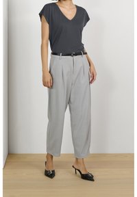 Grå kortærmet V-hals top, parret med løse grå bukser og et sort bælte. Sorte spidse sko med detaljer fuldender outfittet.