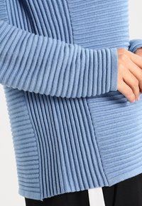 Lyseblå ribbet sweater med strukturerede vertikale og horisontale striber, med tætsiddende ærmer og et glat, blødt stof.