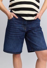 Denimshorts med en afslappet pasform, mørkeblå farve, stil med fem lommer og opsmøgede kanter. Stoffet viser en subtil tekstur og syningsdetaljer.