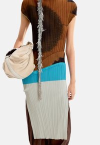 Plisowana sukienka w brązowo-turkusowo-szarym kolorze z metalicznymi frędzlami. W towarzystwie miękkiej beżowej torby.