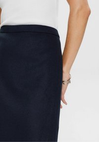 Jupe crayon bleu marine en tissu texturé avec une ceinture lisse, présentant une coupe droite et des détails de couture subtilement visibles.