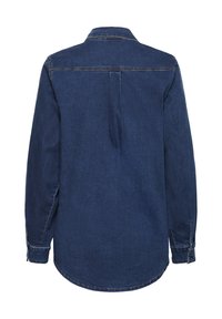 Sötétkék farmering hosszú ujjal, gallérral és gombos mandzsettával. Hátsó redővel rendelkezik a szabadabb mozgás érdekében és ívelt alsó szegéllyel rendelkezik.