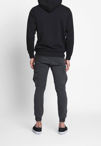 Černá mikina s kapucí v kombinaci s tmavě šedými cargo kalhotami s elastickými manžetami na kotnících a několika bočními kapsami. Černé nazouvací boty dotvářejí celý vzhled.