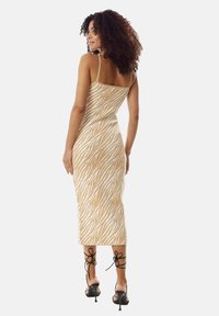 Beige zebra-striped midi dress with thin straps, fitted silhouette, and soft texture, paired with black strappy high-heeled sandals.