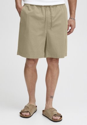 Beige katoenen shorts met een losse pasvorm, verstelbare trekkoord tailleband en zijzakken, gecombineerd met bruine slip-on sandalen.