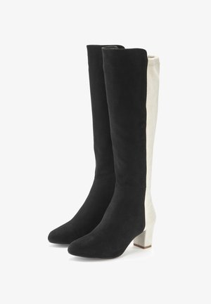 Knöchelhohe Wildlederstiefel mit schwarzer Vorderseite und elfenbeinfarbener Rückseite, Blockabsatz, spitze Zehen und glatter Textur.