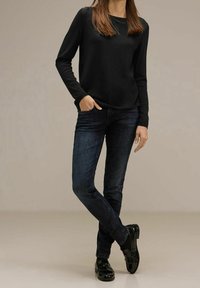 Svart långärmad skjorta i kombination med mörkblåjeans och blanka svarta loafers. Outfiten har en avslappnad passform och minimalistisk design.