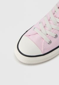 Ροζ καμβάς αθλητικό παπούτσι με λευκό καουτσουκένιο κάλυμμα μύτης, μαύρο περίγραμμα και λευκά κορδόνια. Διαθέτει υφή επιφάνειας και στρογγυλά ανοίγματα για κορδόνια.