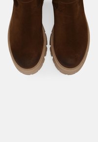 Bruine suede enkellaarzen met een ronde neus, gestructureerd bovenwerk en een dikke beige zool met duidelijke looppatronen.
