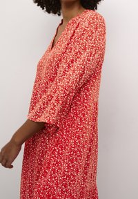 Rød blomsterkjole med V-hals, trekvartærmer og en afslappet pasform. Stoffet har hvide plante mønstre og en blød tekstur.