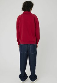 Sweatshirt rouge avec un col montant et des poignets côtelés, associé à un jean en denim sombre ample avec deux poches arrière.