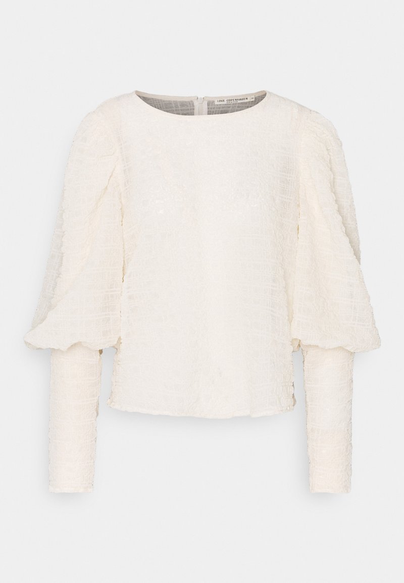 Vit texturerad långärmad blus med rund halsringning och puffärmar, med en synlig dragkedjestängning bak.