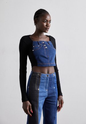 Top nero a coste, tagliato, con maniche lunghe abbinato a salopette in denim, caratterizzata da bottoni e un mix di tessuti blu e neri.