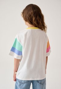 Valge lühikeste varrukatega T-särk, millel on värvilised triibud (mentooli roheline, sinine, roosa, oranž) varrukatel, kollane krae ja pehme tekstuur.