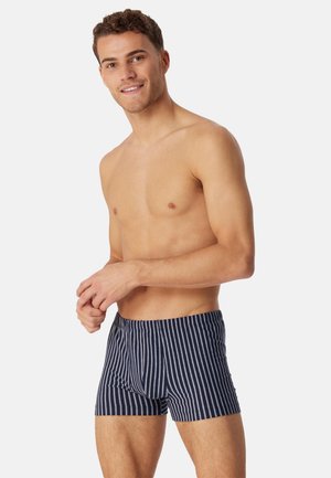 Marineblå badebukser med elastisk talje og striber, der har en glat tekstur og en længde til midt på låret. Striberne er vandret.