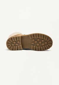 Barna gumicsizma talp hatszögletű tapadásmintázattal, amely masszív barázdákkal és kiemelkedő elemekkel rendelkezik a tapadás érdekében. Puha felső anyag látható.