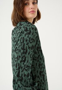 Maglione verde oversize con motivo astratto nero, texture a coste e design con spalla cadente. Adatto per un abbigliamento casual.