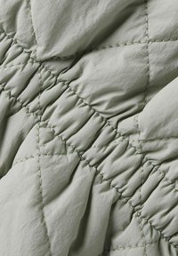 Quilted stof i blød grøn med fremtrædende syede diamantmønster og samlet tekstur, der fremviser et glat, let materiale.