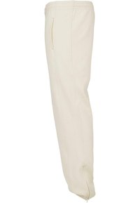 Pantaloni joggers bej din bumbac cu un design conic, având buzunare laterale și fermoare la tivuri, textură netedă și detalii de cusătură vizibile.