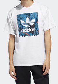Vit bomull t-shirt med en färgglad grafik av Adidas-logotypen i blått och svart med abstrakta virvelmönster, rund halsringning och korta ärmar.