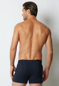 Boxeri din bumbac negru cu un tiv elastic moale, văzuți din spate. Textură netedă, formă ajustată și design minimalist.