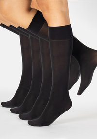 Cinco piernas que llevan calcetas de algodón negro hasta la rodilla y semi-transparentes, ligeramente superpuestas, sobre un fondo claro.