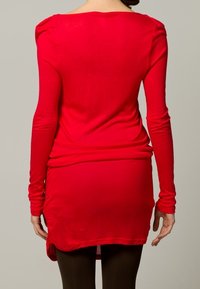 Langärmliges rotes Kleid mit enger Passform, einem runden Ausschnitt auf der Rückseite, strukturiertem Stoff und abgerundetem Saum, kombiniert mit schwarzen Strumpfhosen.