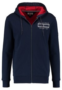 Felpa con zip di colore navy con fodera rossa, cordini con punte decorative e design del logo bianco sul petto. Tessuto morbido.