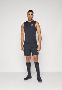 Svart ermeløs treningsskjorte kombinert med svarte shorts og knelange sokker; har en tettsittende design og en liten logo på brystet.