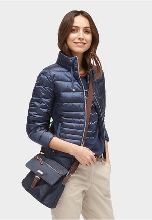 Doudoune bleu marine avec col haut, fermeture éclair à l'avant et coutures horizontales ; associée à un sac bandoulière gris foncé avec des accents marron.